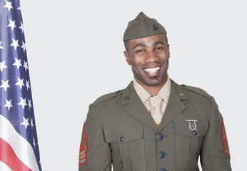 Photo: Portrait of a male US soldier smiling with American flag over gray background Portrait of a male US soldier smiling with American flag over gray background
