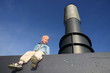 Kleiner Junge sitzt vor einem Schornstein vor blauem Himmel