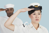 Photo: Portrait of serious female US Navy officer and male sailor saluting over light blue background Portrait of serious female US Navy officer and male sailor saluting over light blue background