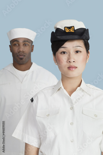 Photo: Portrait of serious female US Navy officer in front male sailor over light blue background Portrait of serious female US Navy officer in front male sailor over light blue background