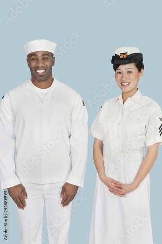 Photo: Portrait of happy female US Navy officer with male sailor over light blue background Portrait of happy female US Navy officer with male sailor over light blue background