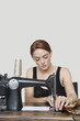 Photo: Young female tailor stitching cloth on sewing machine over colored background Young female tailor stitching cloth on sewing machine over colored background