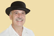 Happy senior man wearing hat while looking up over yellow background