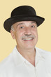 Portrait of happy senior man with black hat over yellow background
