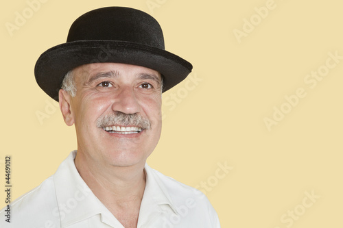 Photo: Happy senior man wearing hat while looking up over yellow background Happy senior man wearing hat while looking up over yellow background