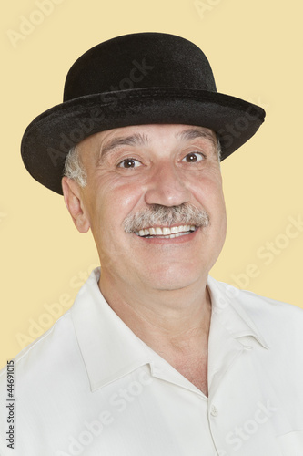 Photo: Portrait of happy senior man with black hat over yellow background Portrait of happy senior man with black hat over yellow background
