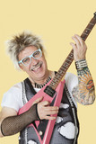 Photo: Portrait of happy senior male punk rock musician playing guitar over yellow background Portrait of happy senior male punk rock musician playing guitar over yellow background