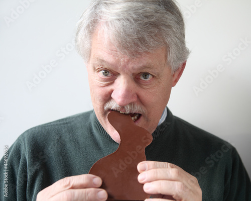 Photo: senior man bites into chocolate Easter rabbit senior man bites into chocolate Easter rabbit