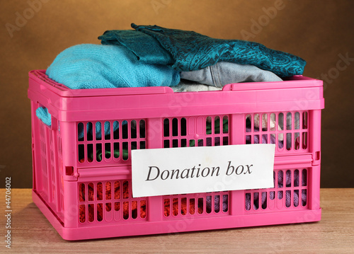 Photo: Donation box with clothing on brown background close-up Donation box with clothing on brown background close-up