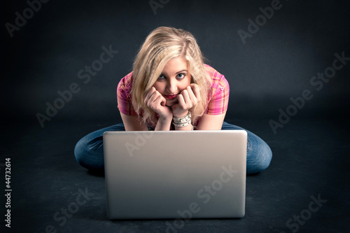 Photo: Pretty girl working on a laptop against black background. Pretty girl working on a laptop against black background.