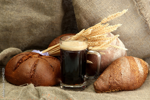 Photo: tankard of kvass and rye breads with ears, on burlap background tankard of kvass and rye breads with ears, on burlap background