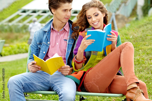 Photo: Couple of students sitting outdoors studying and smiling Couple of students sitting outdoors studying and smiling