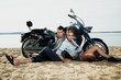 Boyfriend and girlfriend rider sitting on sand beach by bike