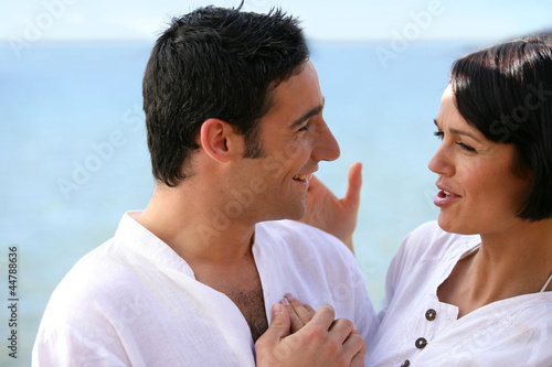 Photo: Playful couple stood talking at the seaside Playful couple stood talking at the seaside