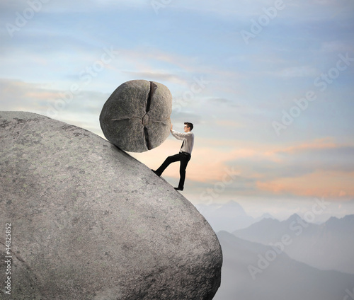 Photo: Businessman pushing a boulder on a rock Businessman pushing a boulder on a rock