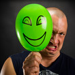 Angry man hiding behind happy balloon