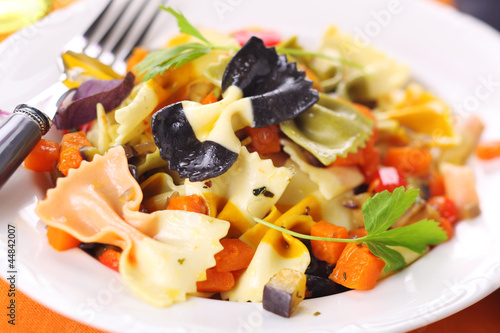 Photo: Pasta farfalle with vegetables on white plate. Pasta farfalle with vegetables on white plate.