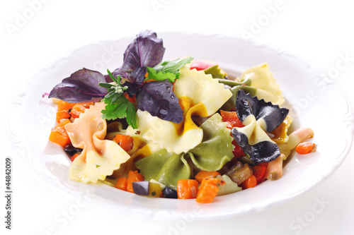 Photo: Pasta farfalle with vegetables on white plate. Pasta farfalle with vegetables on white plate.