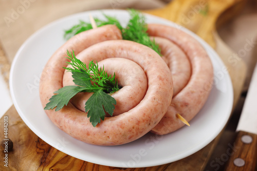 Photo: Raw coiled sausages on wooden board. Raw coiled sausages on wooden board.