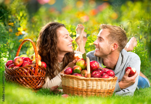 Photo: Couple Relaxing on the Grass and Eating Apples in Autumn Garden Couple Relaxing on the Grass and Eating Apples in Autumn Garden