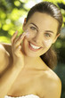 Portrait of young woman putting lotion on cheeks outdoors
