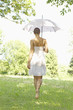 Rear view of young woman walking in grass holding an umbrella