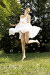 Young happy woman in white dress jumping in midair with bubbles outdoors