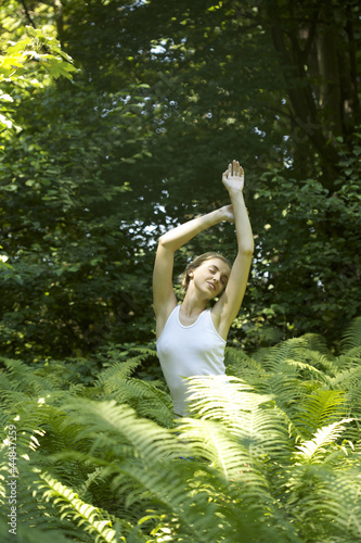 Photo: Portrait of young woman stretching among fern leaves outdoors Portrait of young woman stretching among fern leaves outdoors