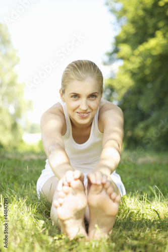 Photo: Portrait of young barefoot woman stretching in grass Portrait of young barefoot woman stretching in grass