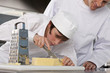 Chef watching trainee slice cheese in commercial kitchen