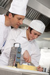 Chef watching trainee slice cheese in commercial kitchen