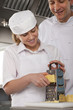 Chef watching trainee grate cheese in commercial kitchen