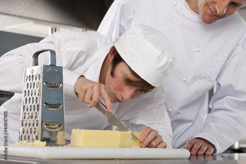 Photo: Chef watching trainee slice cheese in commercial kitchen Chef watching trainee slice cheese in commercial kitchen