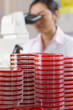 Technician looking into microscope in laboratory with petri dishes in foreground