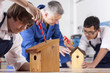 Foto: Teacher watching students attaching roofs to birdhouses in woodworking class Teacher watching students attaching roofs to birdhouses in woodworking class