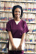 Portrait of smiling nurse holding files in front of medical records on shelves