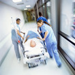 Foto: Doctors in scrubs rushing with patient on hospital gurney through corridor Doctors in scrubs rushing with patient on hospital gurney through corridor
