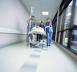 Foto: Doctors in scrubs rushing with patient on hospital gurney through corridor Doctors in scrubs rushing with patient on hospital gurney through corridor