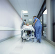 Foto: Doctors in scrubs rushing with patient on hospital gurney through corridor Doctors in scrubs rushing with patient on hospital gurney through corridor