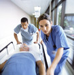 Doctors in scrubs rushing with patient on hospital gurney through corridor