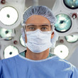 Photo: Close up portrait of surgeon in surgical mask an cap under operating room lamps Close up portrait of surgeon in surgical mask an cap under operating room lamps