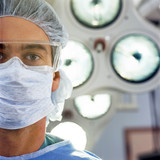 Photo: Close up portrait of serious doctor wearing surgical mask and cap in operating room Close up portrait of serious doctor wearing surgical mask and cap in operating room