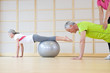 Personal trainer helping senior man balance on fitness ball in exercise class