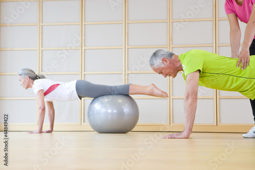 Photo: Personal trainer helping senior man balance on fitness ball in exercise class Personal trainer helping senior man balance on fitness ball in exercise class