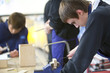 Boy using saw to cut wood in classroom workshop