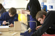 Boy using saw to cut wood in classroom workshop