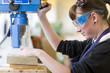 Girl wearing safety goggles and using drill to cut wood in school workshop