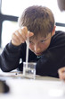 Boy checking liquid temperature with thermometer in laboratory classroom