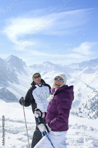 Photo: Portrait of smiling senior couple wearing sunglasses and holding ski poles on snowy mountain Portrait of smiling senior couple wearing sunglasses and holding ski poles on snowy mountain