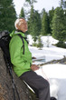 Smiling senior man with backpack, map and compass leaning on tree in snowy woods